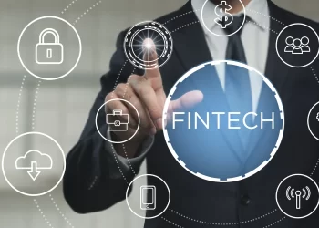 A person in a suit interacts with a virtual touchscreen displaying various technology icons connected by lines. The central icon is labeled “Fintech.” Other icons represent a lock, cloud download, briefcase, MSSP, smartphone, dollar sign, group of people, and Wi-Fi. | FintechZoom