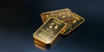 Three gold bars are stacked on a dark surface. The top bar is marked "GLOBAL INTERGOLD" and "100 g FINE GOLD 999.9" with a globe design. The other two bars display similar markings, including "1 OUNCE" and "INMR". These gleaming treasures, echoing the high gold price today, shine brightly reflecting the light. | FintechZoom