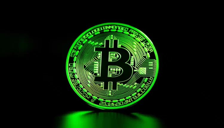 A glowing green Bitcoin symbol stands out in the center of a dark background. The symbol has circuit-like detailing, representing digital currency technology. The vibrant green light reflects on the surface below, creating a neon effect, perfect for anyone looking to buy bitcoin without ID. | FintechZoom