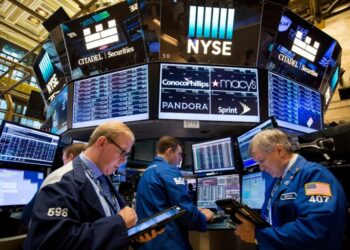 Traders work on the floor of the New York Stock Exchange (NYSE), surrounded by digital screens displaying stock information and company logos including Citadel Securities, ConocoPhillips, Macy's, Pandora, and Sprint—highlighting today's top stock gainers. | FintechZoom