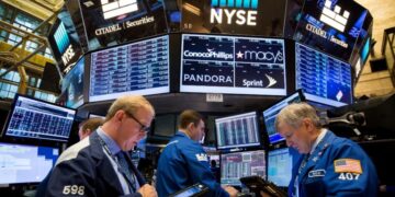 Traders work on the floor of the New York Stock Exchange (NYSE), surrounded by digital screens displaying stock information and company logos including Citadel Securities, ConocoPhillips, Macy's, Pandora, and Sprint—highlighting today's top stock gainers. | FintechZoom