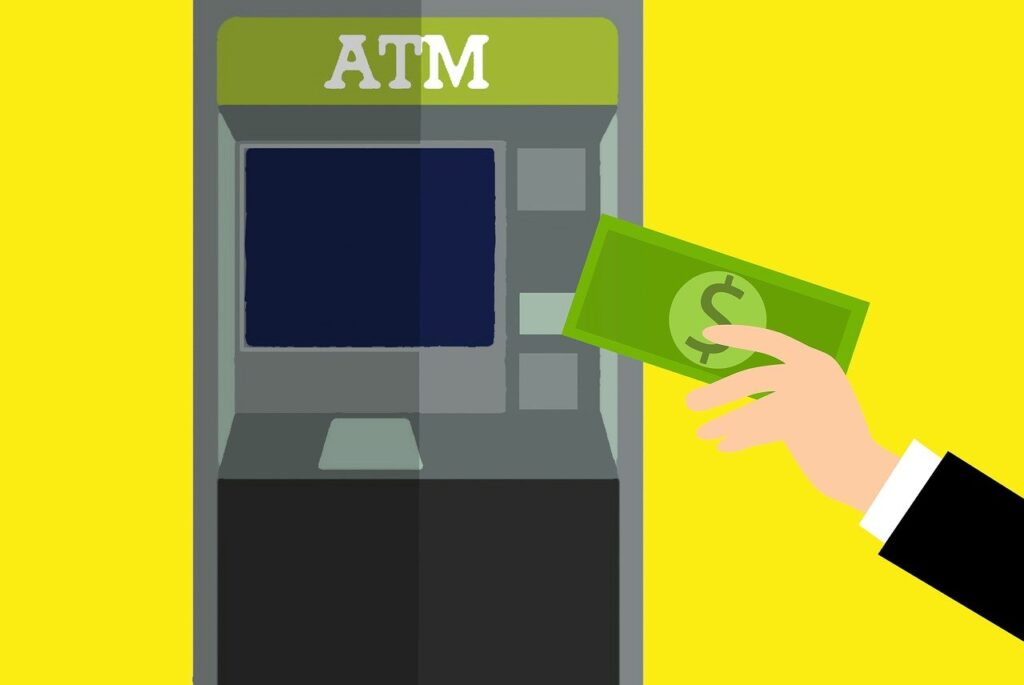 Illustration of an ATM with a person’s hand holding green banknotes near the machine. The ATM screen is blank, and the background is yellow. The hand appears to be inserting or withdrawing money from the ATM. | FintechZoom