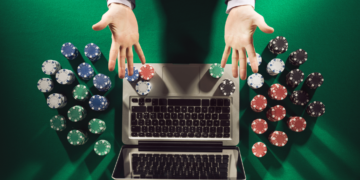 A person in a suit reaches out over a laptop keyboard, surrounded by stacks of poker chips on a green felt surface, suggesting an online gambling scenario through sweepstakes casino apps. | FintechZoom