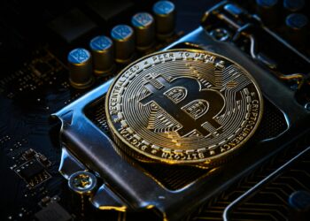 A close-up of a golden Bitcoin coin placed on a computer motherboard, symbolizing the digital and technical nature of cryptocurrency. The coin is prominently displayed, showing detailed engravings, reflecting the rising Bitcoin price in today's market. | FintechZoom