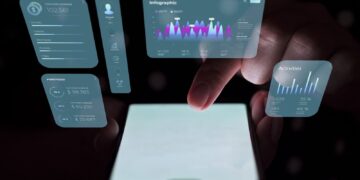 A person uses a web app on their smartphone with holographic data displays projected above it. The holograms show various statistics, charts, and graphs, including communication details, an infographic, portfolio values, and recent activities. The background is dark. | FintechZoom