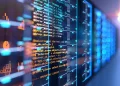 An image of a server rack with multiple units, glowing blue with indicator lights. In the foreground, transparent lines of colorful code are superimposed, representing programming and data processing activities in a technology and data center environment characteristic of the Digital Age. | FintechZoom