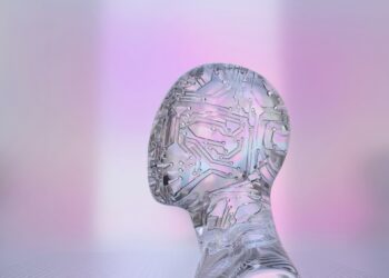 A translucent, futuristic head made of glass or crystal is shown against a soft, blurred background in hues of pink and violet. Embedded with intricate circuit patterns, it symbolizes the integration of technology and human form, much like EssayService AI blending intelligence with creativity. | FintechZoom