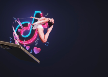 A person in athletic wear performs an aerial split while suspended from a large cellphone. Surrounding them are floating hearts, music notes, and the TikTok logo, all illuminated with colorful neon lights against a dark background—truly capturing the creativity TikTok agencies seek to cultivate. | FintechZoom