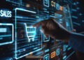 A person’s hand interacts with a digital touchscreen displaying holographic shopping cart and sales icons, representing e-commerce and online shopping. The interface includes various graphs and data visualizations in a futuristic, technological setting, epitomizing the essence of e-commerce evolution. | FintechZoom
