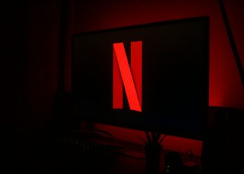 A dark room is illuminated by the red glow of a screen displaying the Netflix logo, highlighting the importance of using the best VPN for streaming to ensure a seamless viewing experience. | FintechZoom