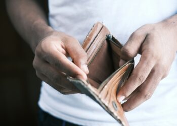 A person wearing a white shirt is holding an open, empty brown wallet with both hands, symbolizing the need for debt consolidation. The background is blurred, focusing on the wallet and the person's hands. | FintechZoom