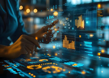 A person interacts with a futuristic digital interface displaying graphs and data visualizations in a dimly lit environment. The screens show analytics with glowing blue and orange elements, suggesting advanced technology use. | FintechZoom