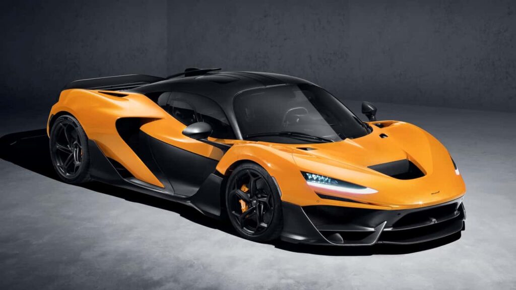 A sleek, modern McLaren W1 sports car with a bright orange body and black accents is parked in a dimly lit space, highlighting its aerodynamic design and detailed features. | FintechZoom