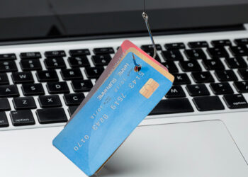 A credit card hangs on a fishing hook above a laptop keyboard, symbolizing phishing scams and online financial fraud. | FintechZoom