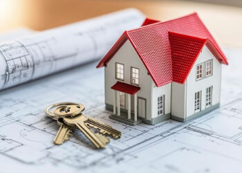 A model of a white house with a red roof sits atop architectural blueprints. To the left, a set of silver keys with a keychain is placed on the blueprints, symbolizing home ownership or real estate planning, highlighting insights from FintechZoom.com Real Estate. | FintechZoom