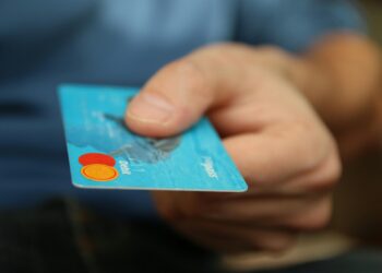 A person holds out a blue credit card, extending it forward. The card is shown in focus, while the background and hand are slightly blurred. | FintechZoom