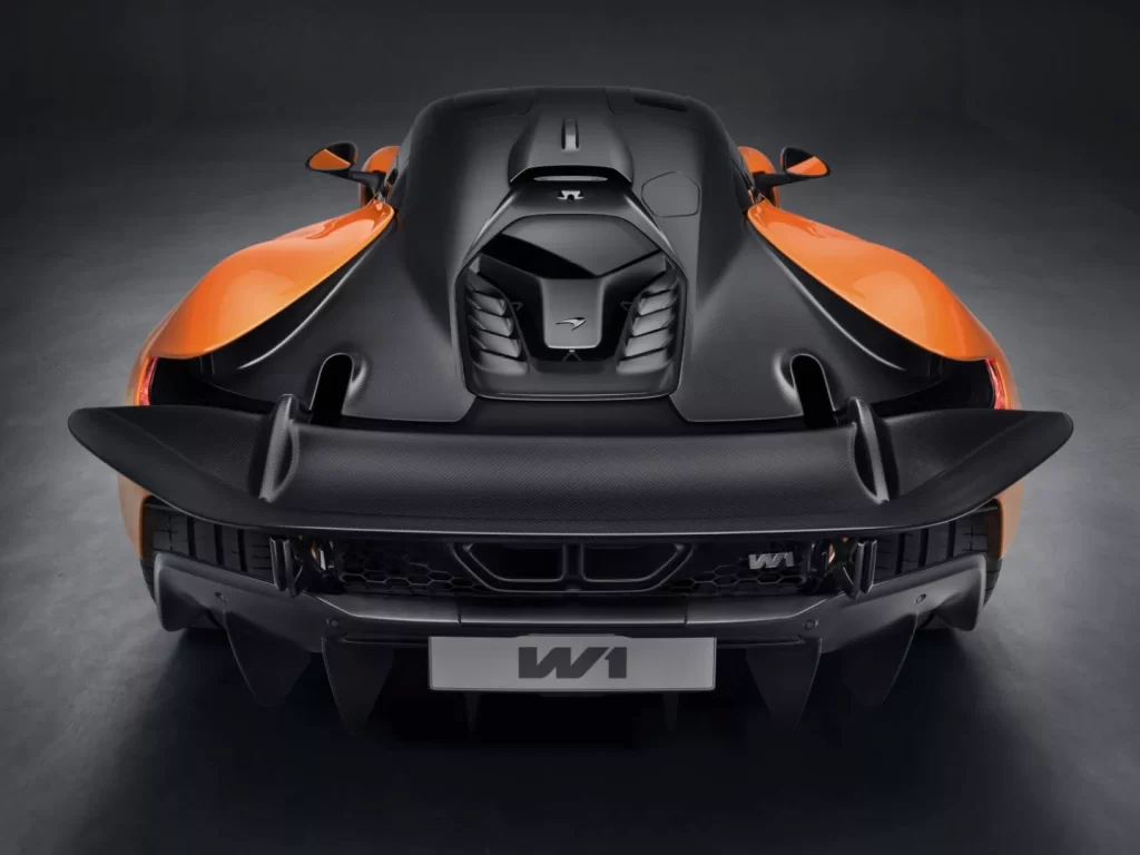 Rear view of an orange and black sports car with sleek, aerodynamic lines and a broad spoiler. The focus is on the McLaren W1's back, boasting a distinctive license plate and detailed design elements under a soft spotlight. | FintechZoom