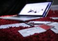 A laptop sits open on a red carpet with various credit cards and receipts scattered in front of it, suggesting online shopping or financial management. | FintechZoom