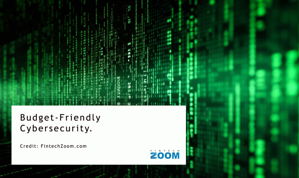 Green digital code on a dark background resembling a matrix style fills the image. A white text box in the lower left corner reads "Budget-Friendly Cybersecurity." Credit is given to FintechZoom.com. | FintechZoom