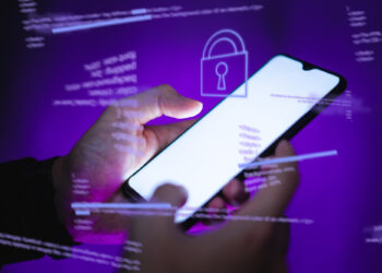 A person holds a smartphone with a lock icon displayed on the screen, hinting at encrypted messaging. Surrounding it are semi-transparent computer code lines, set against a purple background, evoking themes of cybersecurity and encryption. | FintechZoom