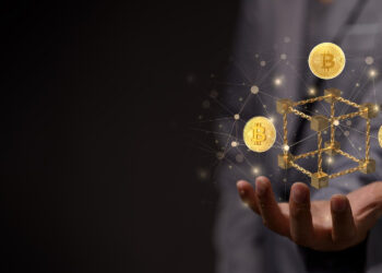 A person in a suit holds a glowing 3D cube with digital connections, surrounded by floating golden Bitcoin symbols, embodying the question from FintechZoom.com: Can DeFi Revolutionize Finance? | FintechZoom