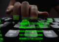 A close-up of a hand typing on a keyboard, with green digital numbers and codes overlaid, resembling a computer hacking scene. The dark background emphasizes the glowing green text, hinting at underlying security strategies in action. | FintechZoom