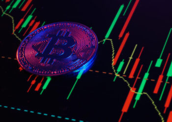 A Bitcoin coin stands on a digital screen from FintechZoom.com, displaying a fluctuating stock chart with red and green candlesticks, symbolizing cryptocurrency market activity alongside insights into crypto trading strategies. | FintechZoom