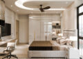 Modern bedroom with neutral tones features a large bed, wall-mounted TV, and sleek built-in wardrobe with glossy doors. A wooden desk and swivel chair sit by the window, and a ceiling fan is centrally mounted in a recessed circular ceiling design. | FintechZoom