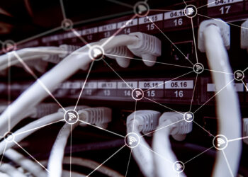 A network server with numerous white Ethernet cables connected to ports. An overlay graphic of interconnected Wi-Fi symbols suggests data transfer and connectivity, emphasizing technology and communication links through German IP addresses. | FintechZoom