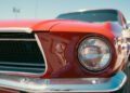 Close-up of a red vintage car's front, showcasing its round headlight, chrome bumper, and part of the grille. With a clear blue sky as a backdrop, this classic beauty invites you to modernize your old car while keeping timeless charm alive in an outdoor setting. | FintechZoom