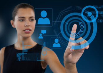 A woman engages with a digital interface, touching a circular graphic with her finger. Icons of people and binary code hover in blue on the dark background, reflecting an advanced virtual environment for seamless customer interaction and lead prospecting. | FintechZoom