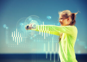 A woman in a bright yellow long-sleeve shirt smiles while holding a dumbbell under a clear blue sky. Futuristic digital graphics, including waves and data charts, overlay the image, illustrating the stock market trends in health and wellness. | FintechZoom