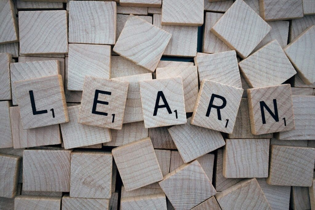 Wooden letter tiles arranged to spell the word "LEARN" on a scattered background of blank tiles. | FintechZoom