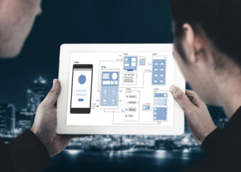 Two people hold a tablet displaying a flowchart of a mobile app interface, illustrating the journey to build an app. The screen reveals interconnected app screens, set against a blurred cityscape background. | FintechZoom