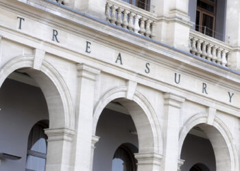 The neoclassical facade resembles that of the Bank of England, with large stone arches. Above the arches, "TREASURY" is prominently displayed in capital letters, and balconies with balustrades adorn the upper level. | FintechZoom