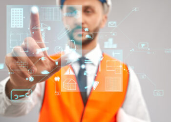 A man wearing an orange safety vest is pointing at a digital interface with various technology and construction icons, including buildings, gears, and tools, symbolizing automation and innovation in construction. | FintechZoom