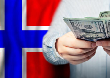 A person is holding a stack of U.S. dollar bills with a Norwegian flag in the background, symbolizing the financial opportunities and consolidation loans available in Scandinavian countries. | FintechZoom