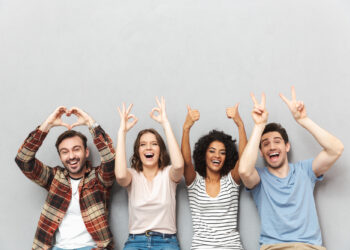 Four people sit against a light gray background, smiling and making hand gestures: a heart with hands, OK sign, thumbs up, and peace sign. Their casual flannel and t-shirts echo a relaxed vibe, embodying the spirit of openness and support crucial for mental health. | FintechZoom