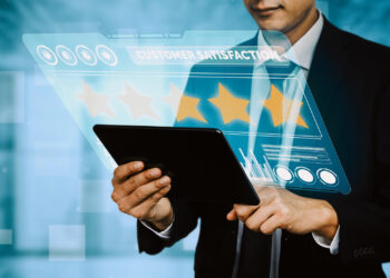 A person in a suit holds a tablet displaying a virtual interface for reputation management. The screen shows a five-star rating with the text "Customer Satisfaction." In the blurred background, it all contributes to a modern, tech-focused atmosphere. | FintechZoom