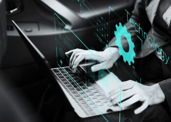 A person types on a laptop amidst transparent digital interfaces displaying graphics, including the words "Technology" and "IT Automation." The setting appears to be a vehicle interior, highlighting the seamless integration of mobile technology. | FintechZoom