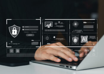 Hands typing on a laptop with a digital overlay of security icons, graphs, and AI elements, highlighting themes of cybersecurity and data protection. | FintechZoom