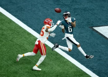A Philadelphia Eagles player in a green and white uniform leaps to catch a pass in the end zone while a Kansas City Chiefs defender tries to block him. The intense scene unfolds on the field with the end zone just within reach. | FintechZoom