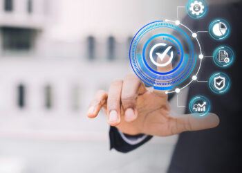 A person in a suit touches a virtual screen displaying a digital checkmark and business-related icons, symbolizing technology, AML compliance, quality assurance, and effective data management. | FintechZoom