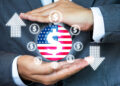 A person in a suit holds their hands around a dollar symbol on an American flag, with dollar icons and arrows, representing financial shifts as Japan firms turn to equity financing amid US tariff pressure. | FintechZoom