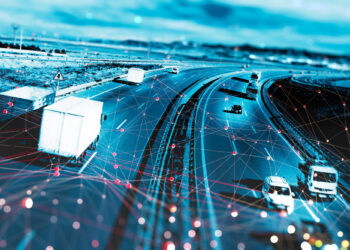 A digitally enhanced image of trucks and cars driving on a highway, overlaid with a network of red and blue lines and dots, representing data connectivity or smart transportation technology. | FintechZoom