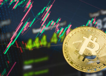 A gold Bitcoin coin in the foreground with digital stock charts and fluctuating red and green candlestick graphs on a dark screen in the background, representing cryptocurrency trading on BYDFi Crypto Exchange. | FintechZoom