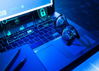 A laptop keyboard with eyeglasses, pens, and a notebook nearby shows digital cybersecurity graphics—lock icons and data charts—projected above the keys, symbolizing data protection and how anonymous casino sites are revolutionizing privacy in online gambling. | FintechZoom