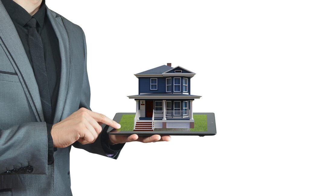 A man in a suit holds a tablet displaying a 3D image of a two-story house with a porch, suggesting long-distance real estate or smart home technology, against a white background. | FintechZoom