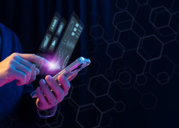 A person in a suit uses a smartphone, with holographic financial and data charts related to modern in-game payments projecting from the screen against a dark background with hexagonal patterns. | FintechZoom