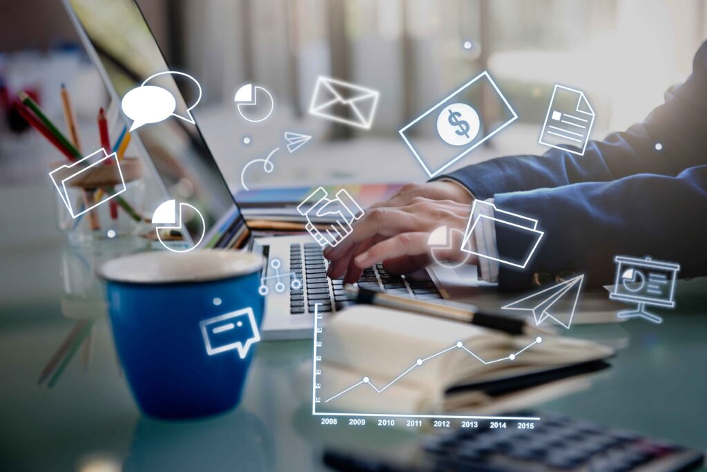 Person typing on a laptop at a desk with a blue cup, notebook, and calculator. Overlaid digital icons represent emails, charts, messages, money, data analysis, and customer acquisition strategies. | FintechZoom